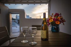 A table with two wine glasses and a bottle of wine, a vase with flowers, and a view of buildings and a sunset.