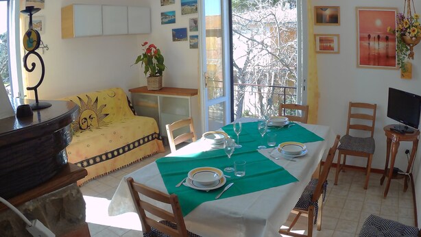 A dining area with a table set for four, chairs, a sofa, and a TV.