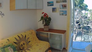 A room with a yellow sofa, a small table with a plant, and a view of a garden through a glass door.