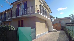 A two-story house with a balcony, a green gate, and a paved driveway.