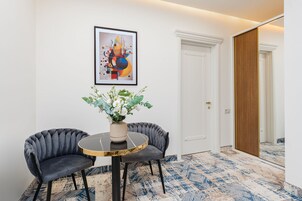 Een kamer met een ronde tafel, twee stoelen, een vaas met bloemen, een lijst met een abstract schilderij en een kamerbreed tapijt met een patroon.