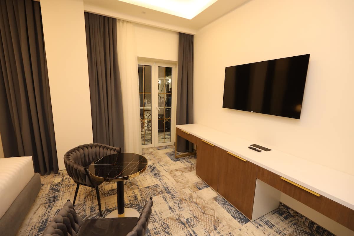 A hotel room with a bed, a round table, a chair, a TV, and a sliding door leading to a balcony.