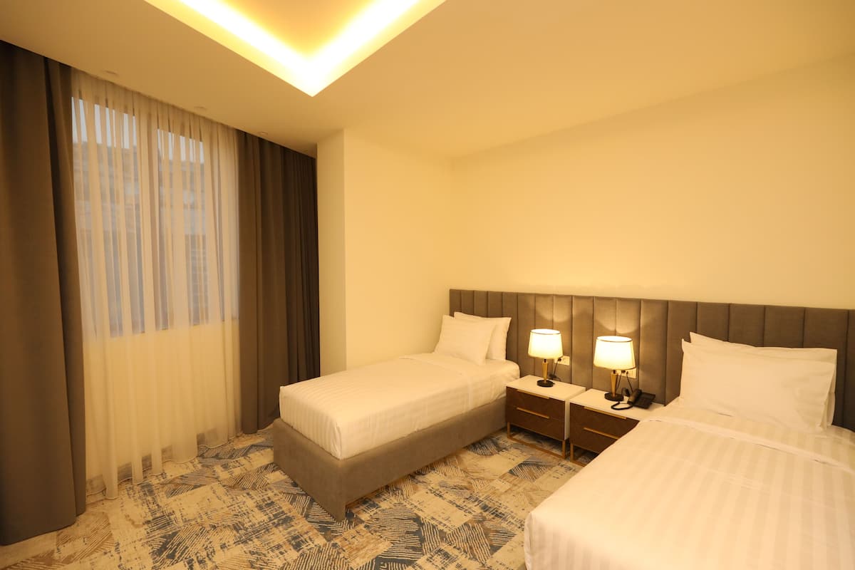 A hotel room with two beds, a nightstand with lamps, a headboard, and a patterned carpet.