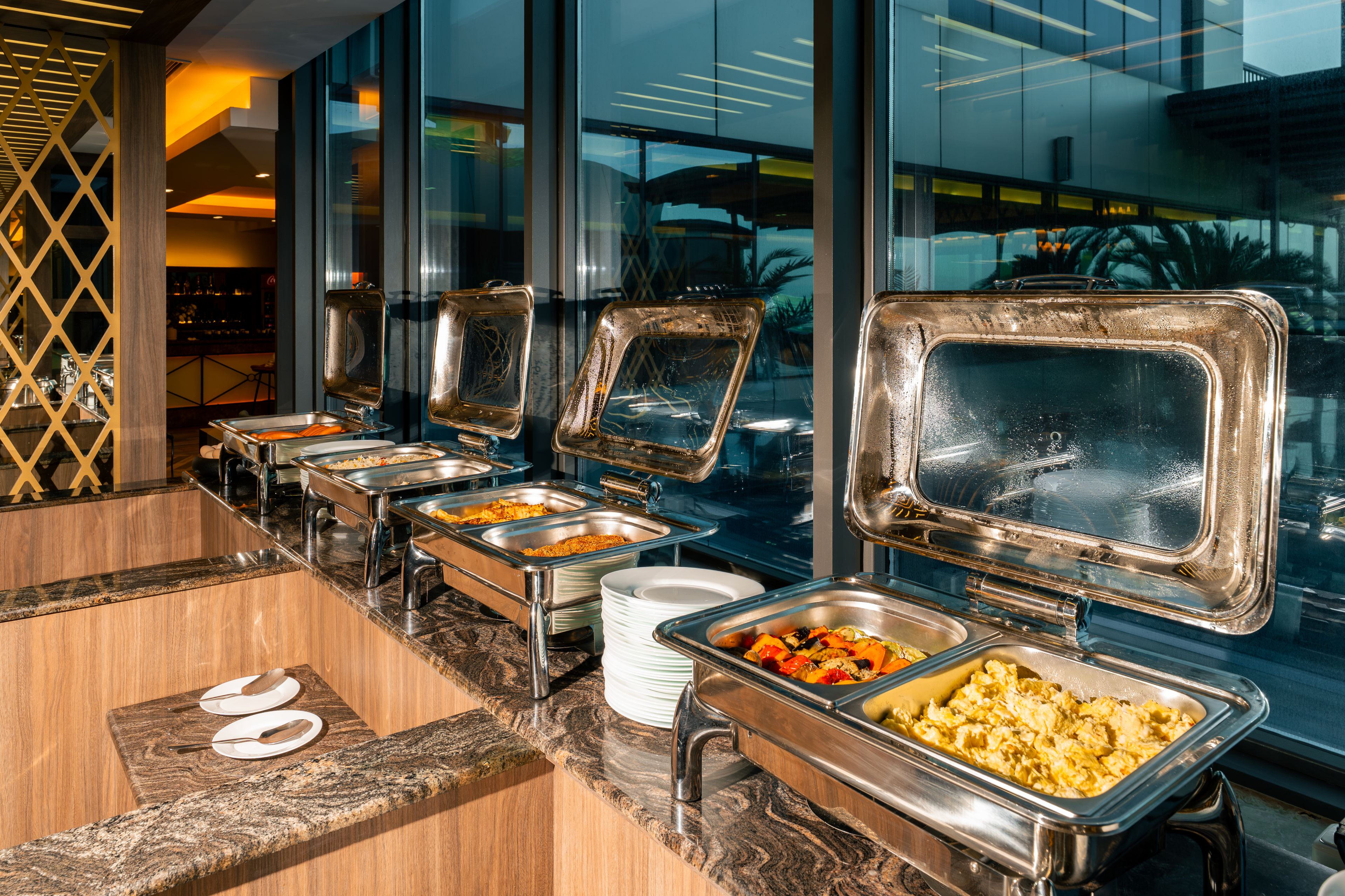 A buffet setup with multiple serving stations, each with a metal tray and a glass cover.
