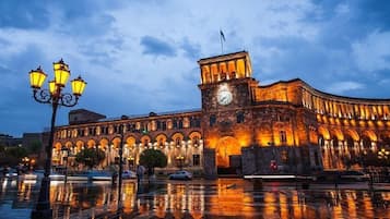 Un bâtiment historique doté d’une tour horlogée, de fenêtres en arc de cercle et d’une surface d’eau qui reflète l’image du bâtiment à l’avant.