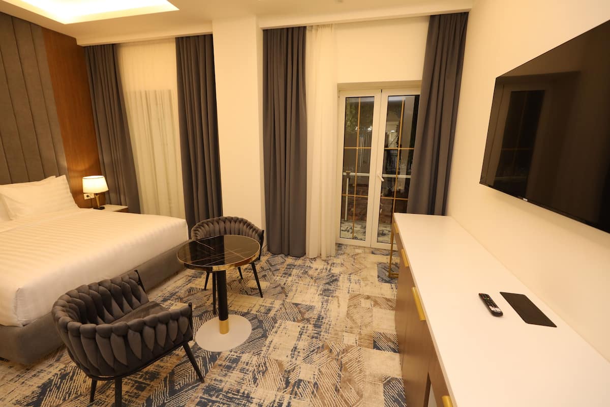 A hotel room with a bed, a desk, a chair, a TV, and a view through a glass door.