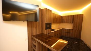 A modern kitchen with a flat-screen TV mounted on the wall, wooden cabinetry, and a sleek countertop.