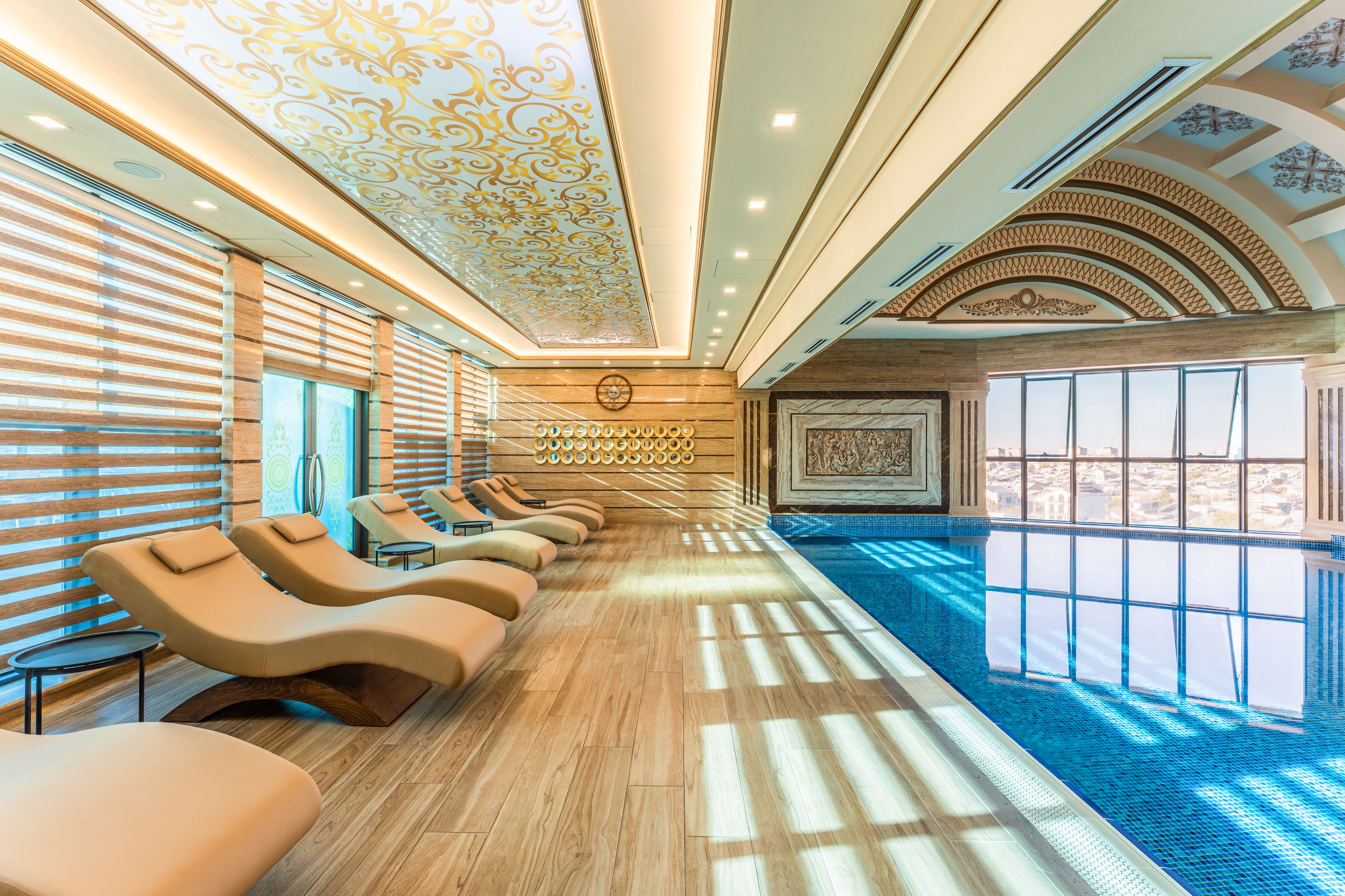 Quarto ensolarado com piscina, cadeiras reclináveis e teto decorado.