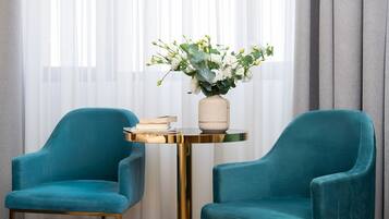 To turkise lænestole, et rundt bord med en vase blomster og en stak bøger.