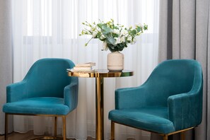 Two teal armchairs, a small round table with a vase of flowers, and a stack of books.