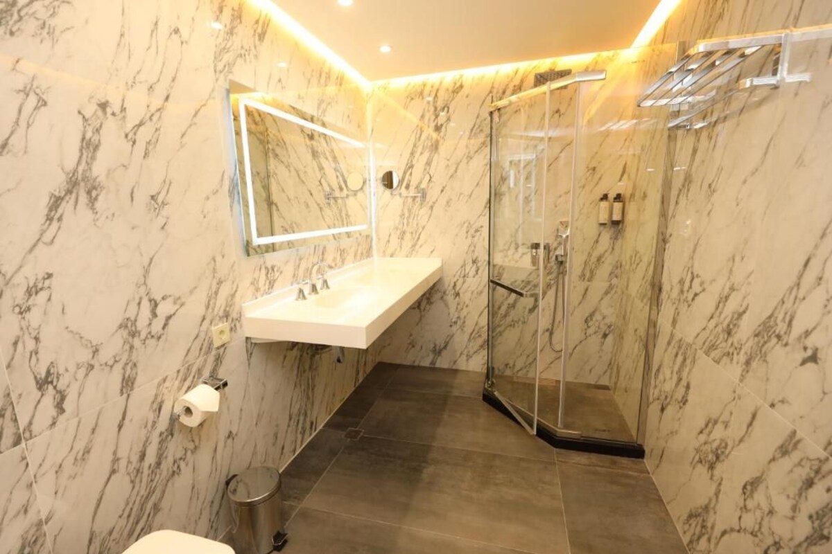 A bathroom with a marble wall, a glass shower enclosure, a white sink, and a toilet.