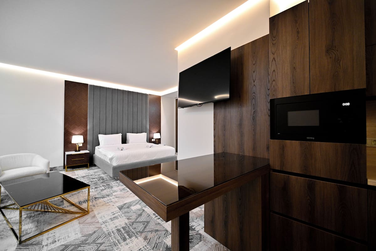 A modern hotel room with a bed, bedside table, lamp, and a flat-screen TV mounted on the wall.