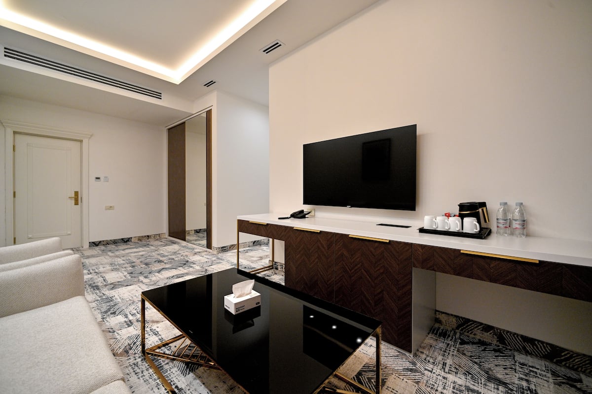 A hotel room with a flat-screen TV, a desk with a coffee maker, and a sofa.