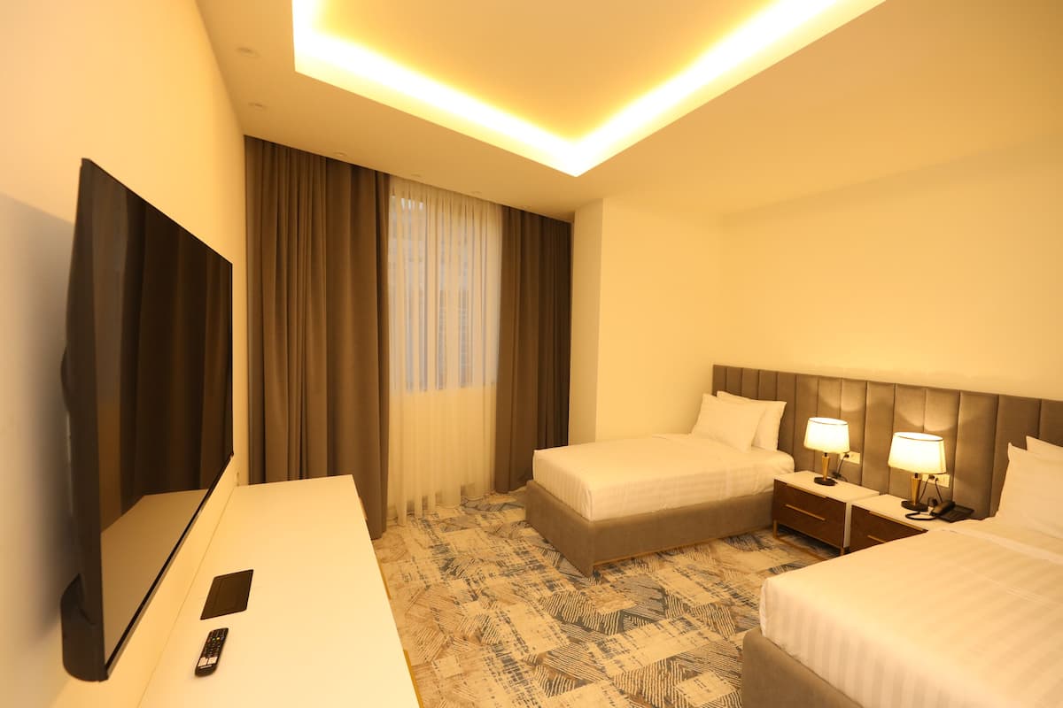 A hotel room with two beds, a TV, a desk, and a remote control.