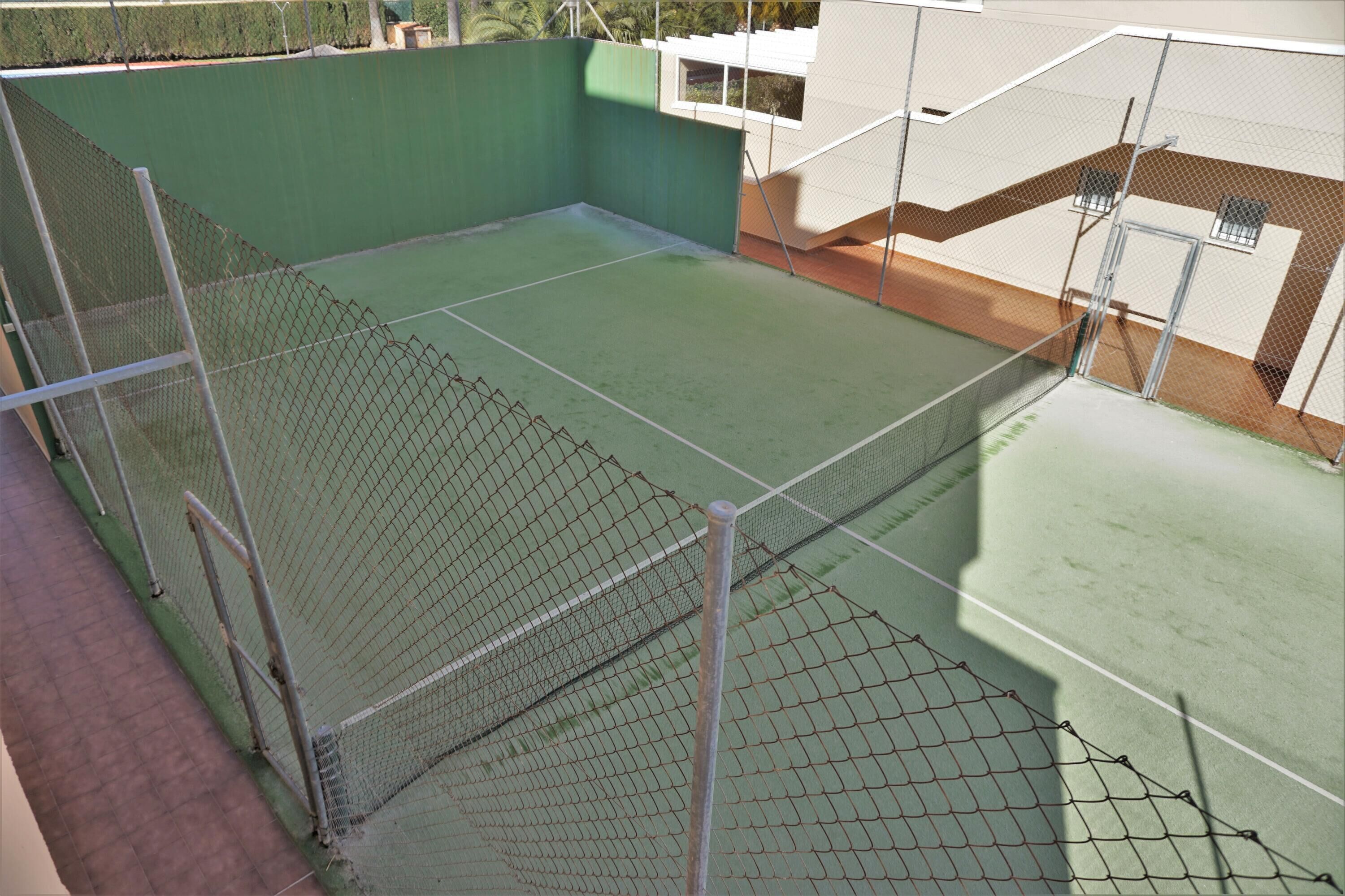 A tennis court with a net and surrounding fence, adjacent to a building with a window and a door.