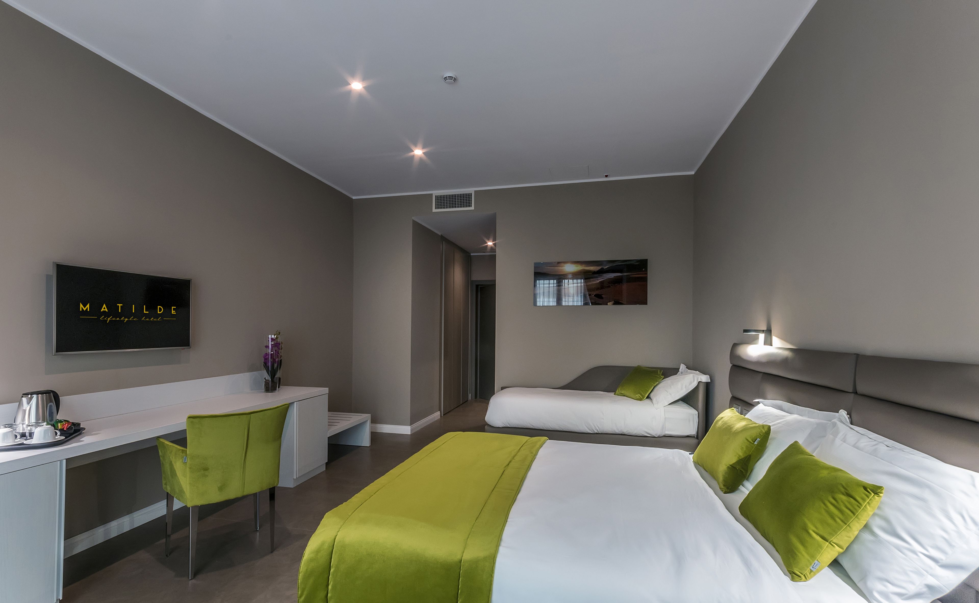 Una habitación de hotel moderna con una cama, un escritorio y una silla. Hay un televisor en la pared y un cuadro sobre la cama.