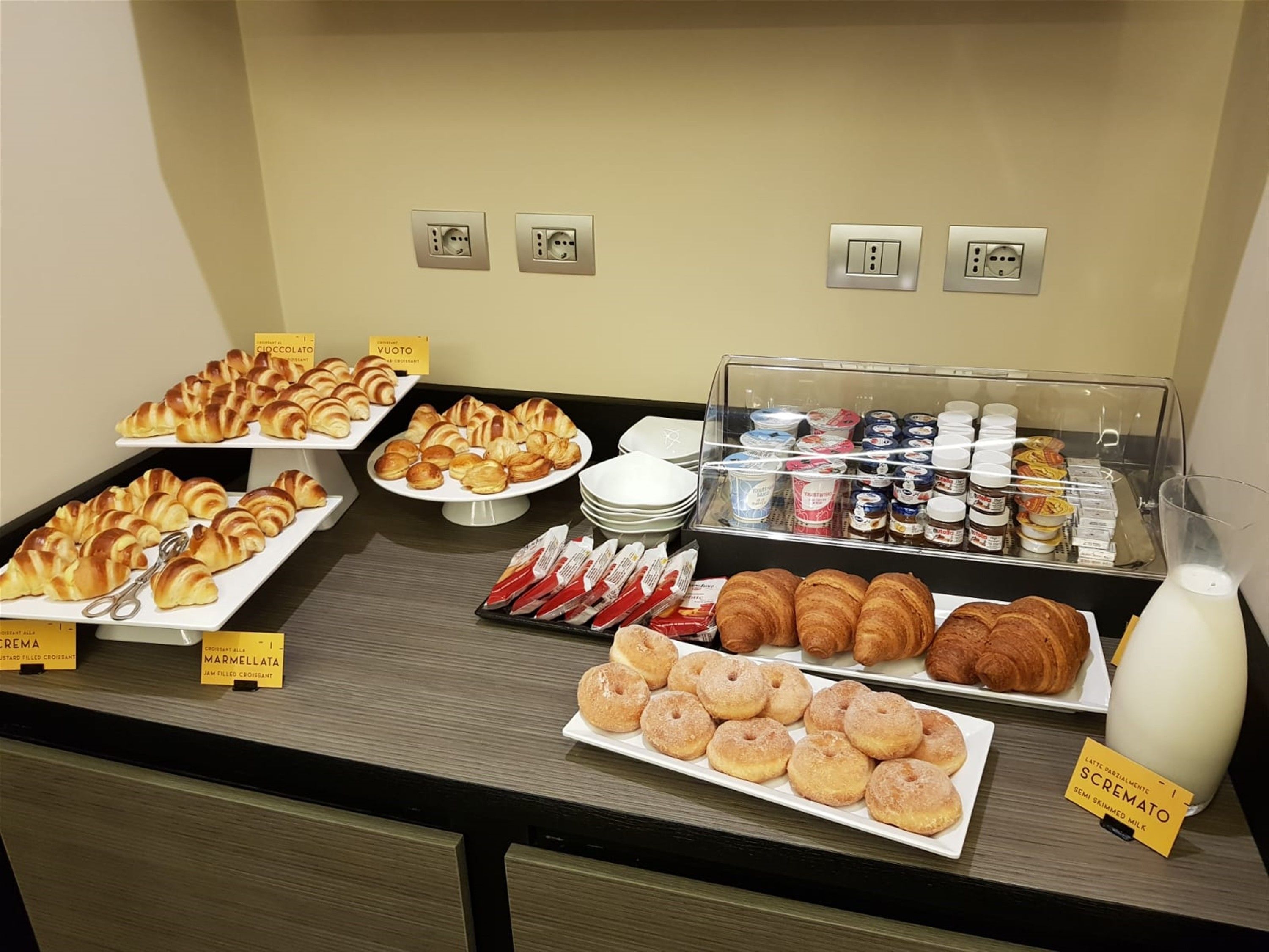 A buffet with various pastries, including croissants and donuts, and a selection of beverages and condiments.
