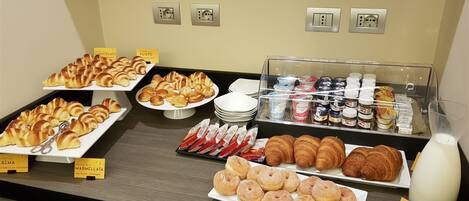 A buffet with various pastries, including croissants and donuts, and a selection of beverages and condiments.