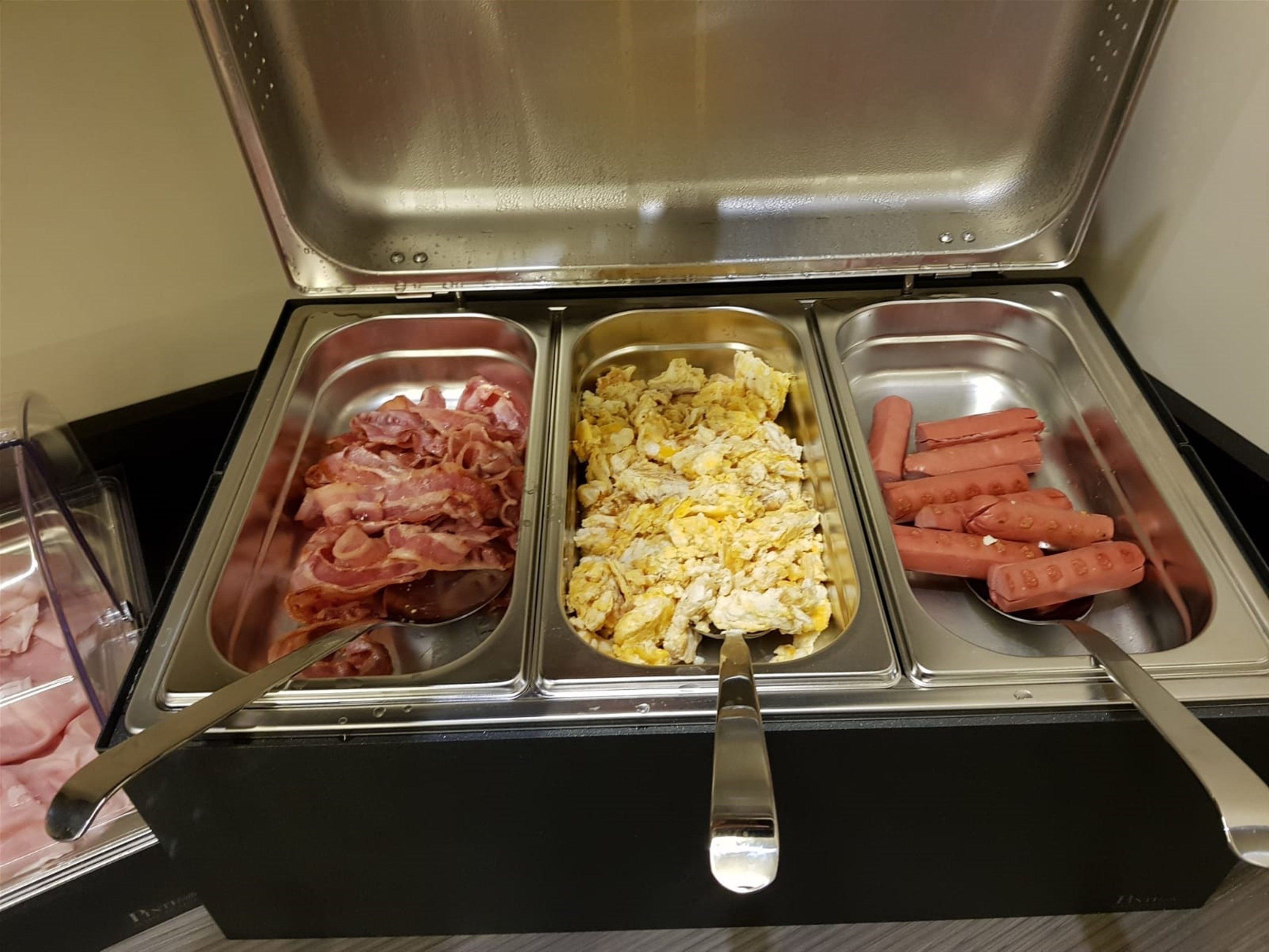 A buffet with three food stations: bacon, scrambled eggs, and hot dogs.