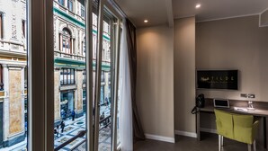 A hotel room with a large window offering a view of a historic building. There's a desk with a laptop, a chair, and a TV mounted on the wall. - Hotel Matilde - Lifestyle Hotel (Naples)