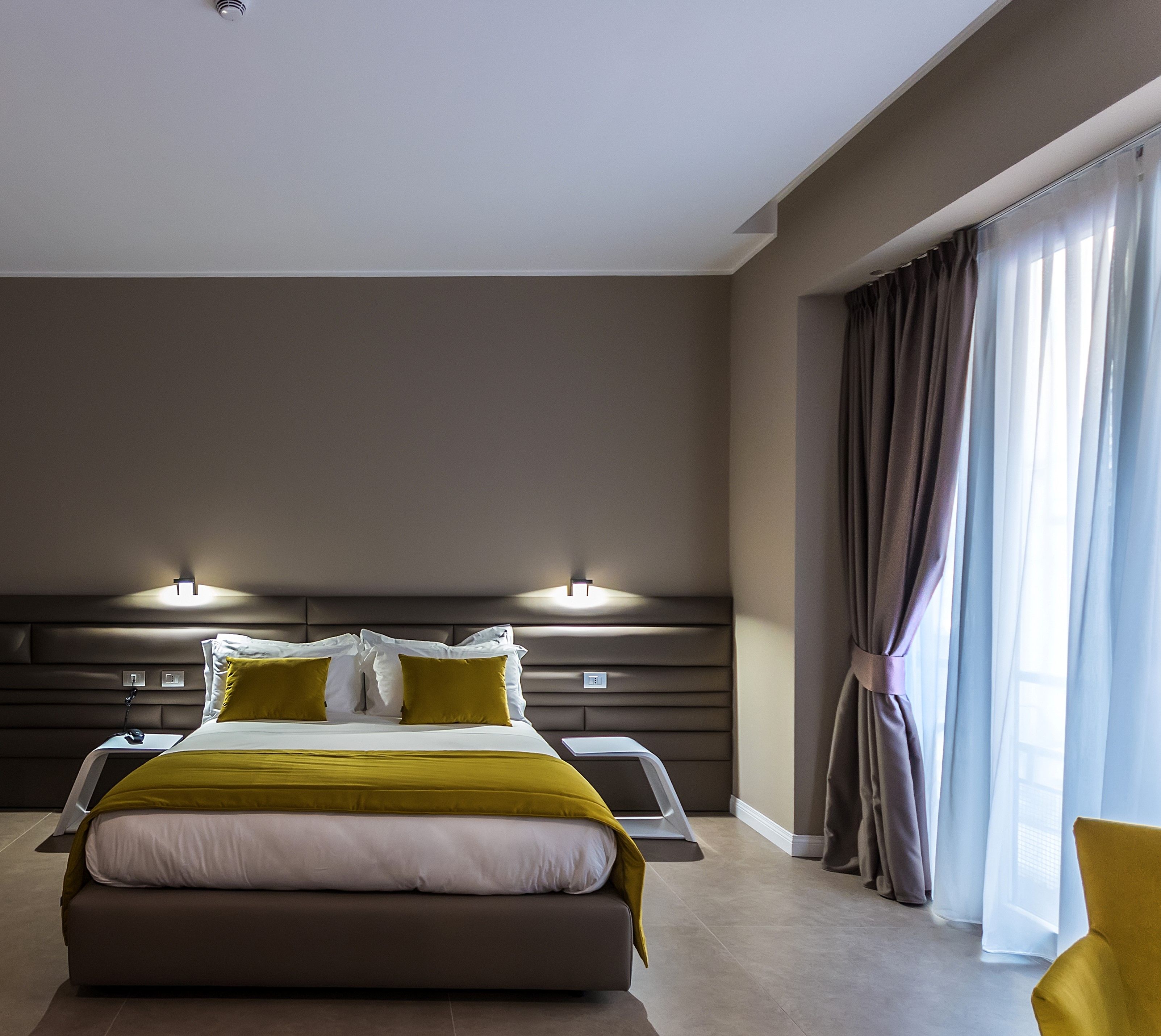 Une chambre d’hôtel moderne avec un grand lit, une table de chevet, une chaise et une fenêtre avec des rideaux.