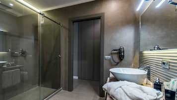 Casa de banho moderna com chuveiro de vidro, um lavatório grande com espelho e um secador de cabelo fixado na parede.