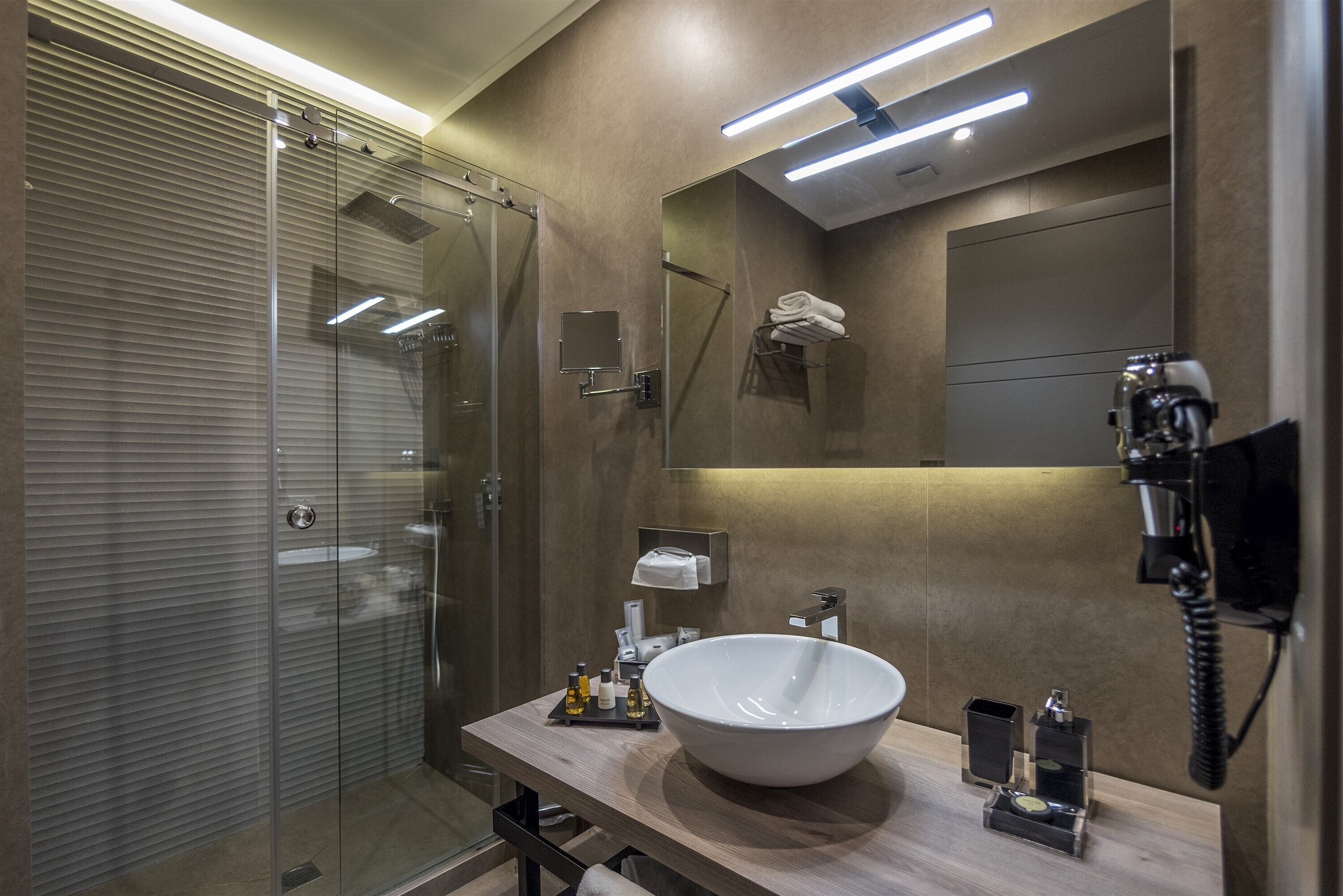 A modern bathroom with a glass-enclosed shower, a large white sink, and a mirror with a towel rack.