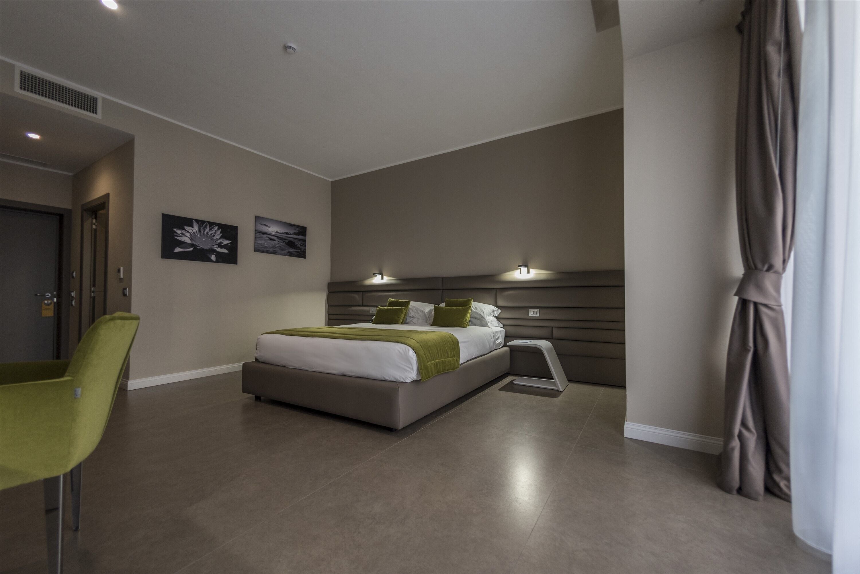 A modern hotel room with a large bed, a green chair, and artwork on the walls.