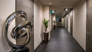 A modern hallway with a large metallic sculpture, potted plants, and a long corridor leading to a seating area. - Hotel Matilde - Lifestyle Hotel (Naples)