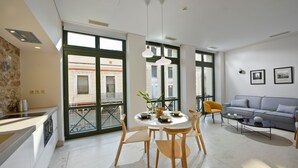 Un salon moderne avec un canapé gris, une table à manger avec des chaises et un balcon offrant une vue sur les immeubles.