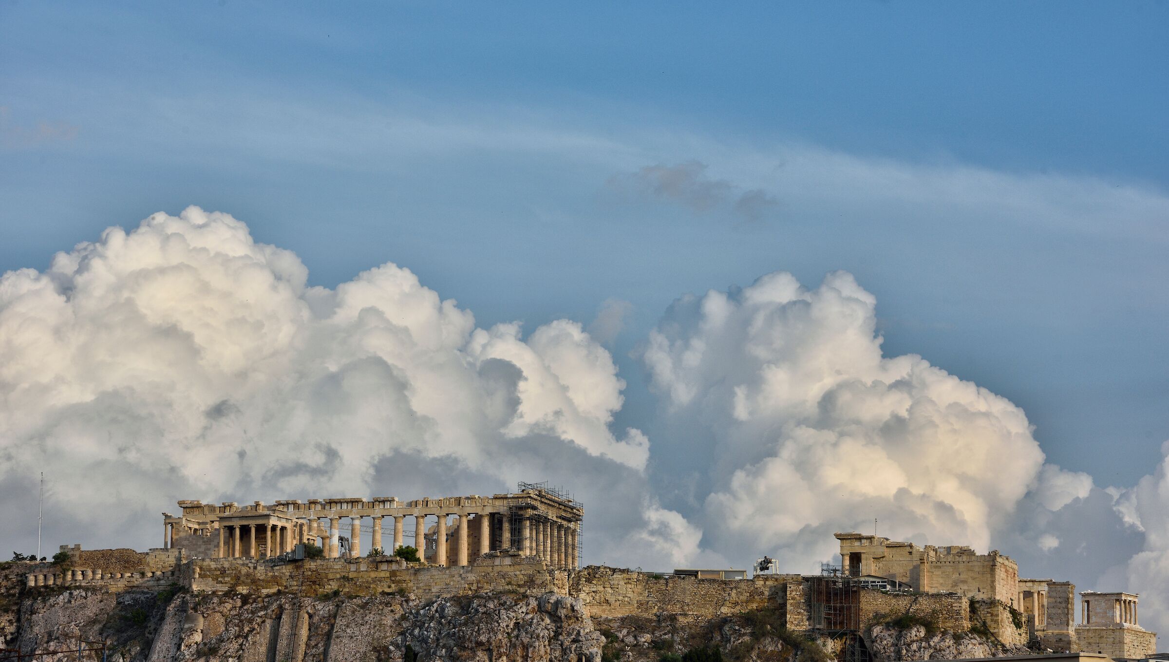 Ancient ruins with columns and a partially reconstructed building, set against a backdrop of large clouds.