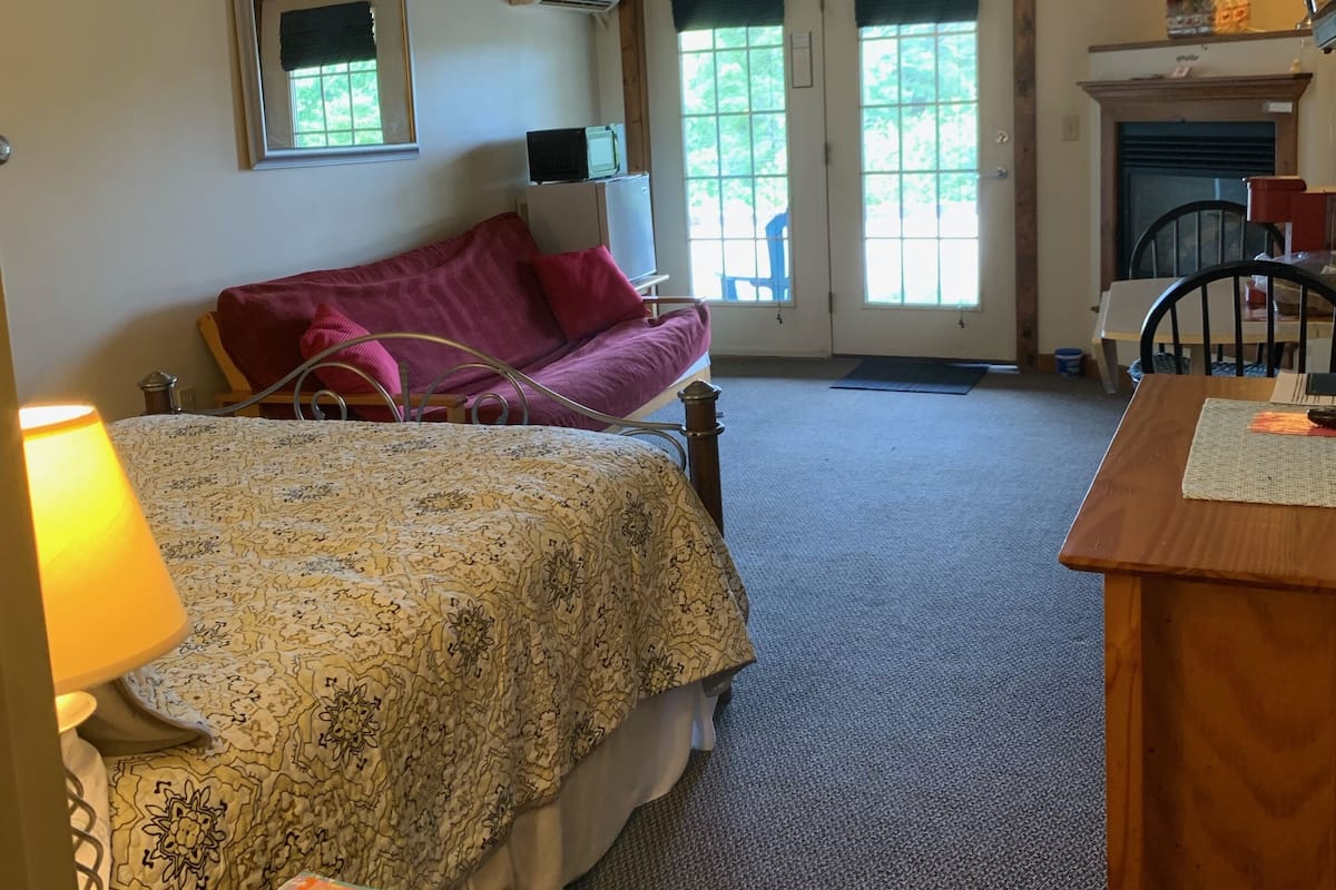 A bedroom with a bed, a desk, a chair, a television, and a fireplace.