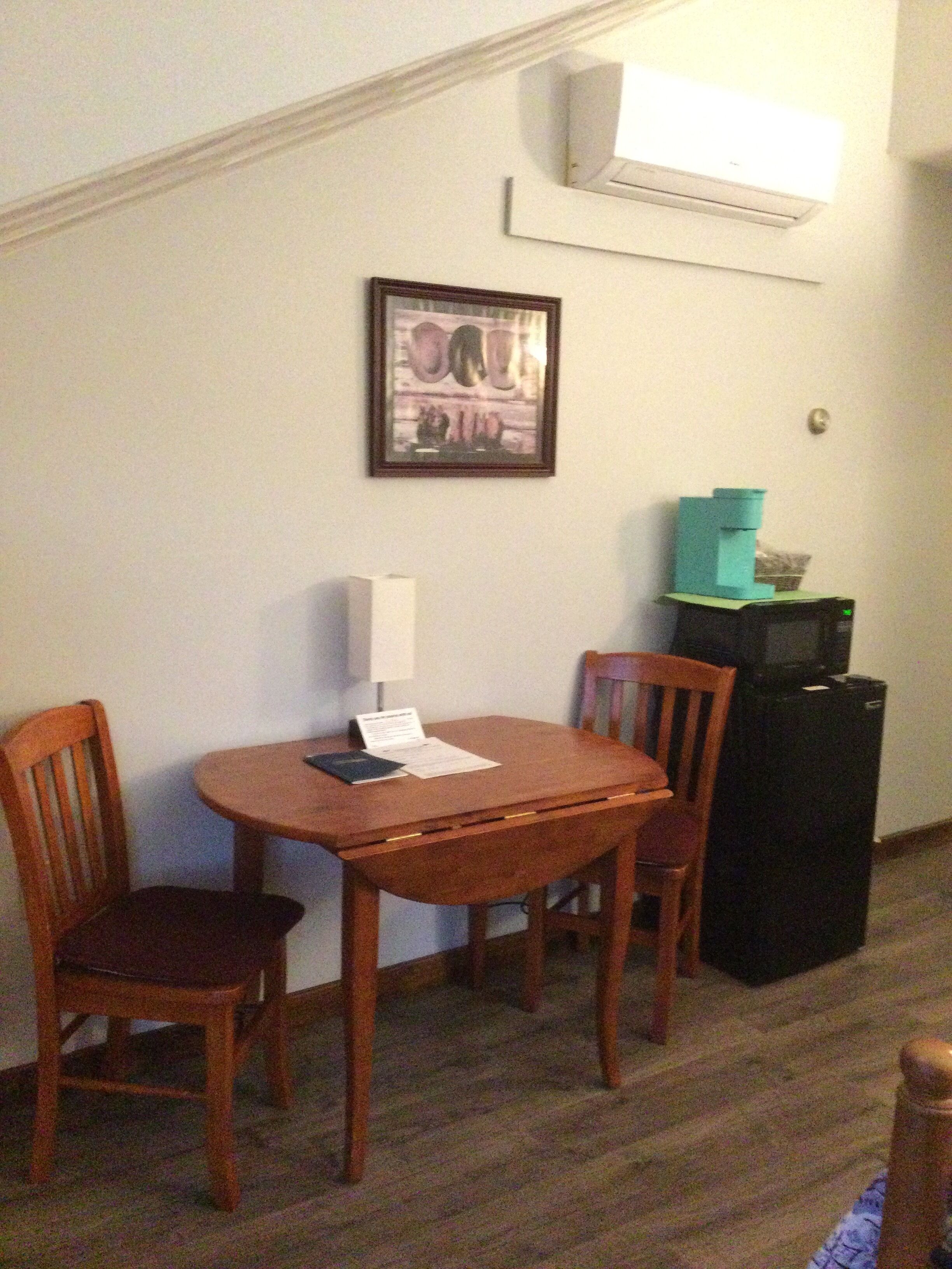A dining area with a wooden table and chairs, a framed picture on the wall, and a black refrigerator.