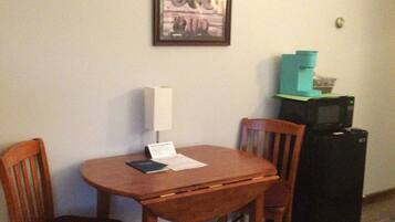 A dining area with a wooden table and chairs, a framed picture on the wall, and a black refrigerator.