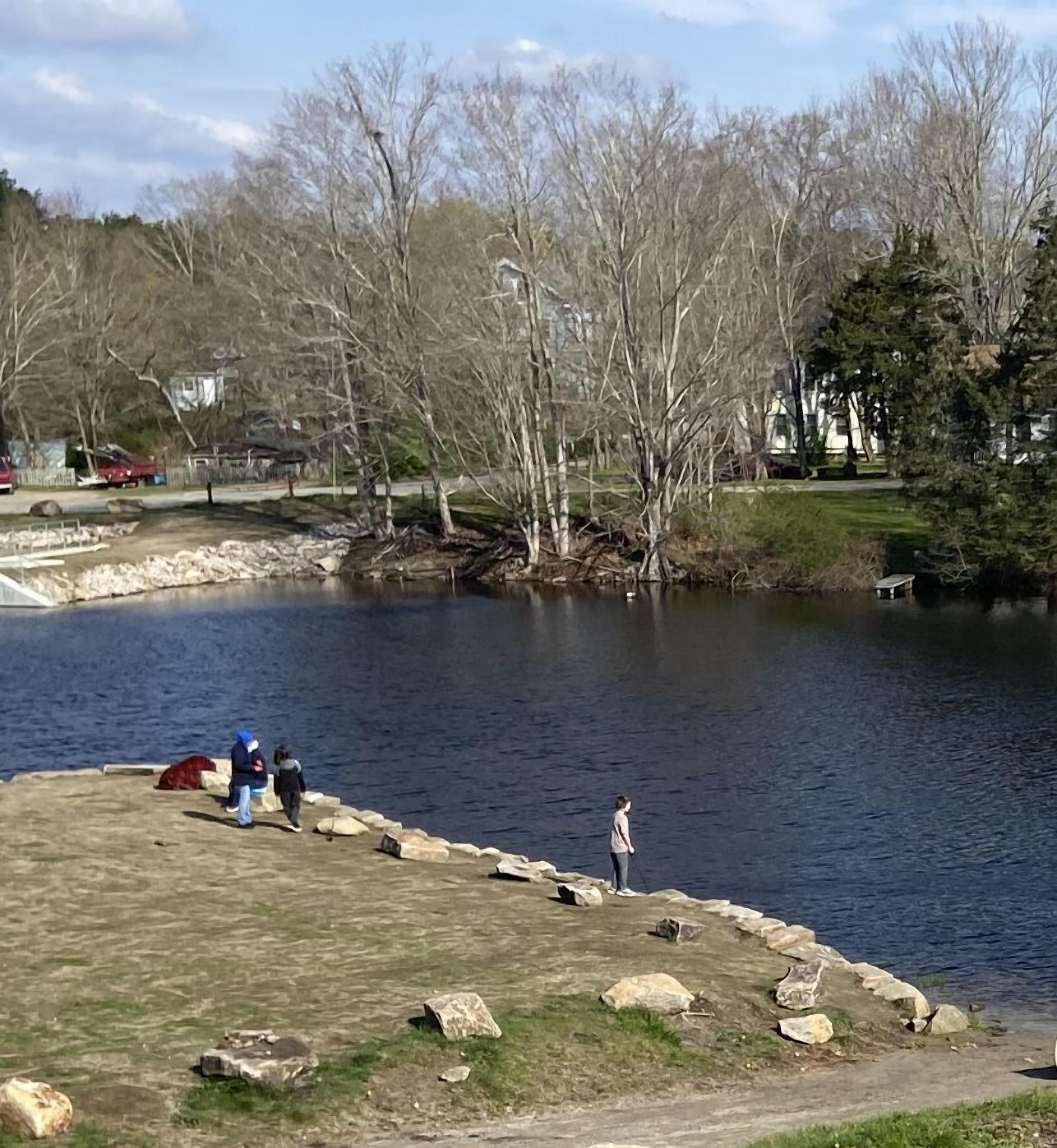 A lakeside park with a grassy area, a stone pathway, and a few people.