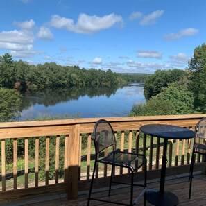 Une terrasse en bois avec une table et des chaises, donnant sur une rivière paisible bordée d’une végétation luxuriante.