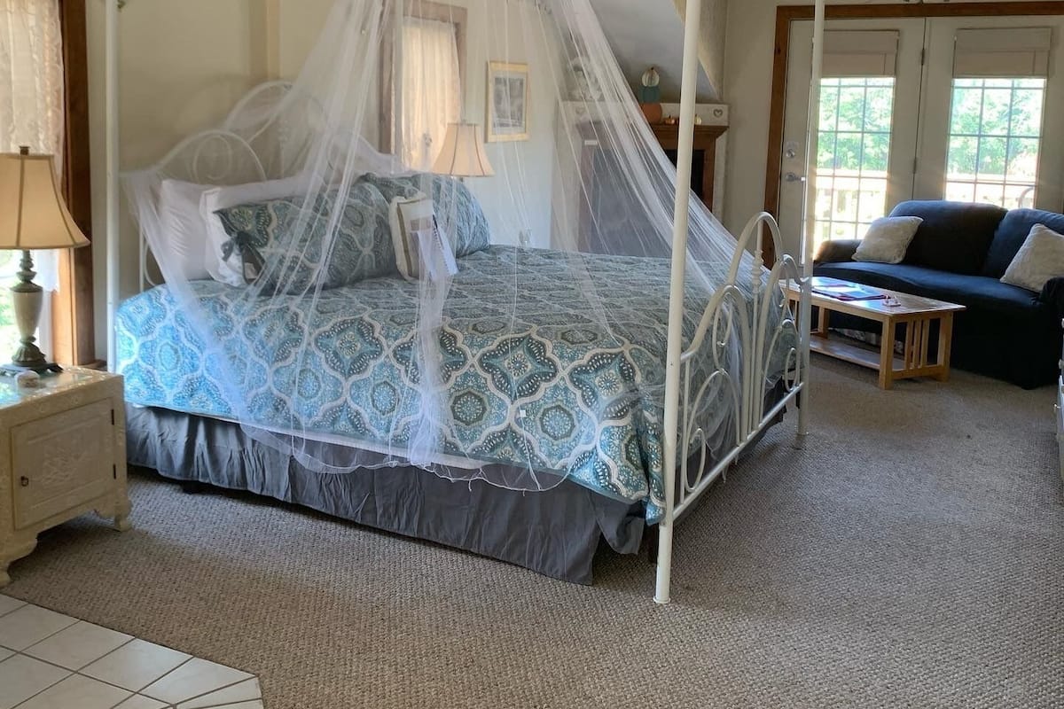 A bedroom with a four-poster bed, a canopy, a nightstand, a bedside table, a sofa, and a window with curtains.