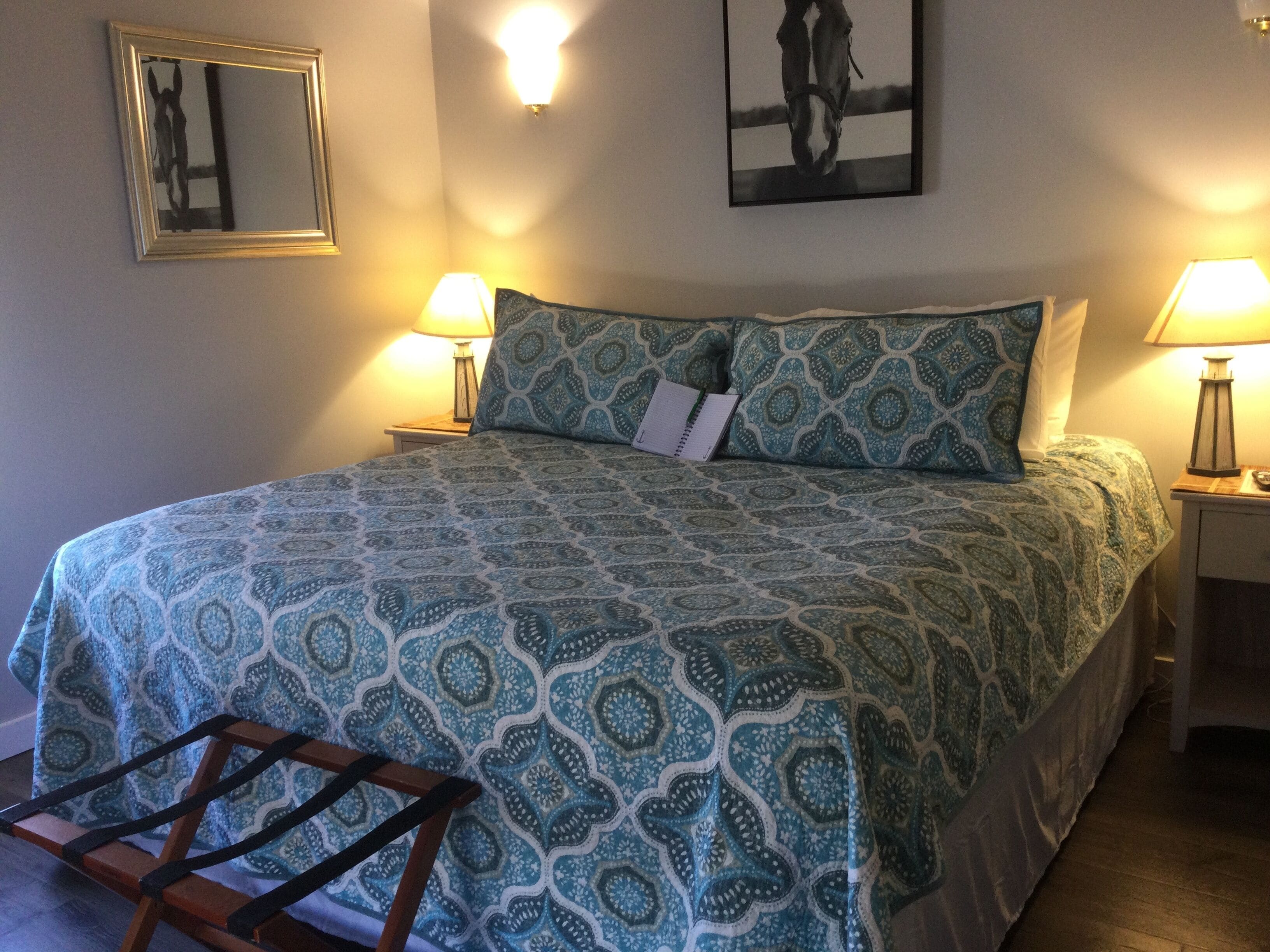 Een opgemaakt bed met behang, twee bedlampjes, een lijst met een foto aan de muur en een spiegel.