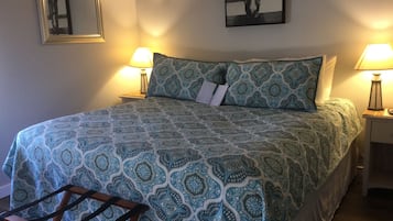 Een opgemaakt bed met behang, twee bedlampjes, een lijst met een foto aan de muur en een spiegel.