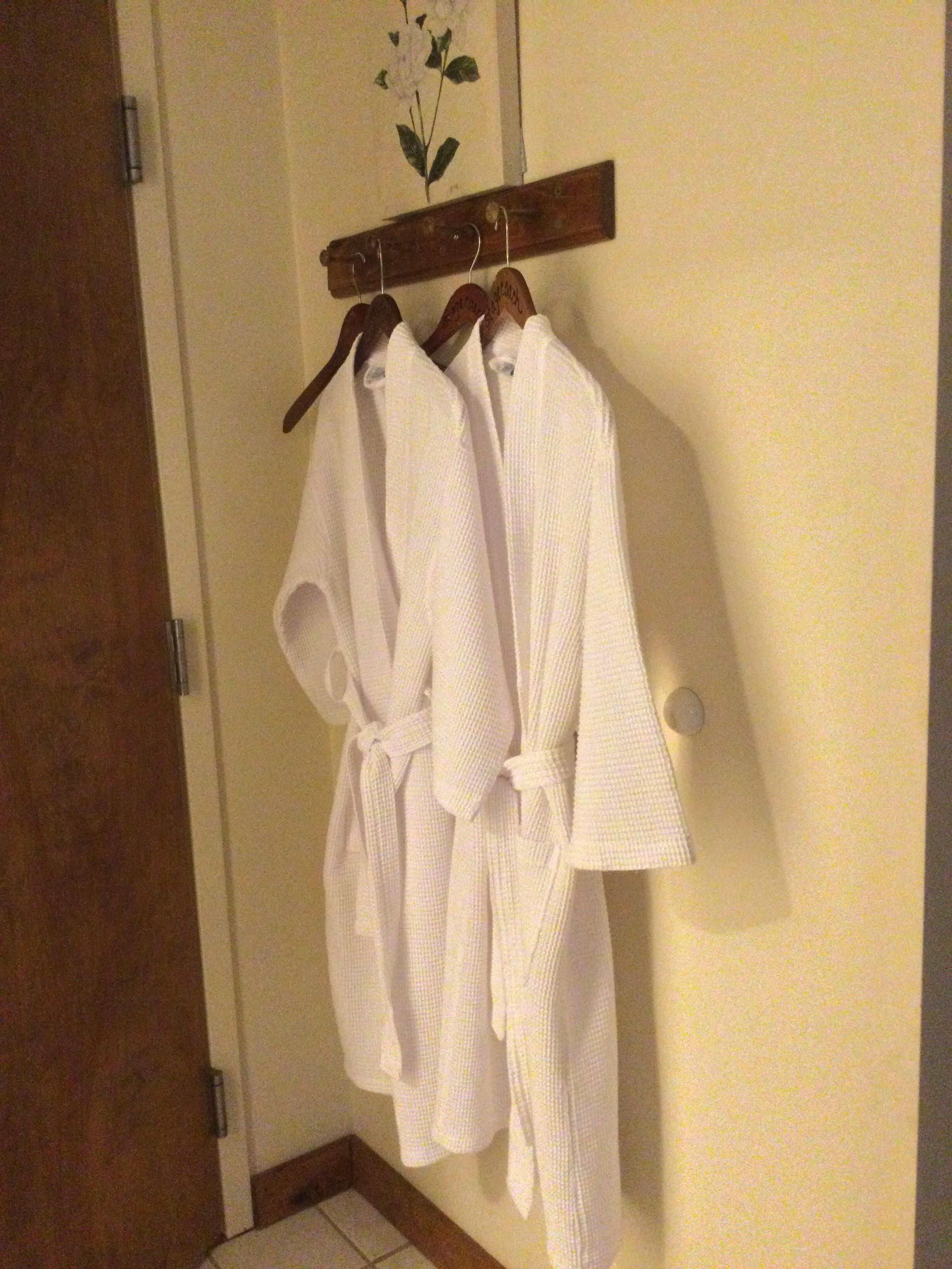 Dos albornoces blancos colgados en un perchero de madera en un baño.