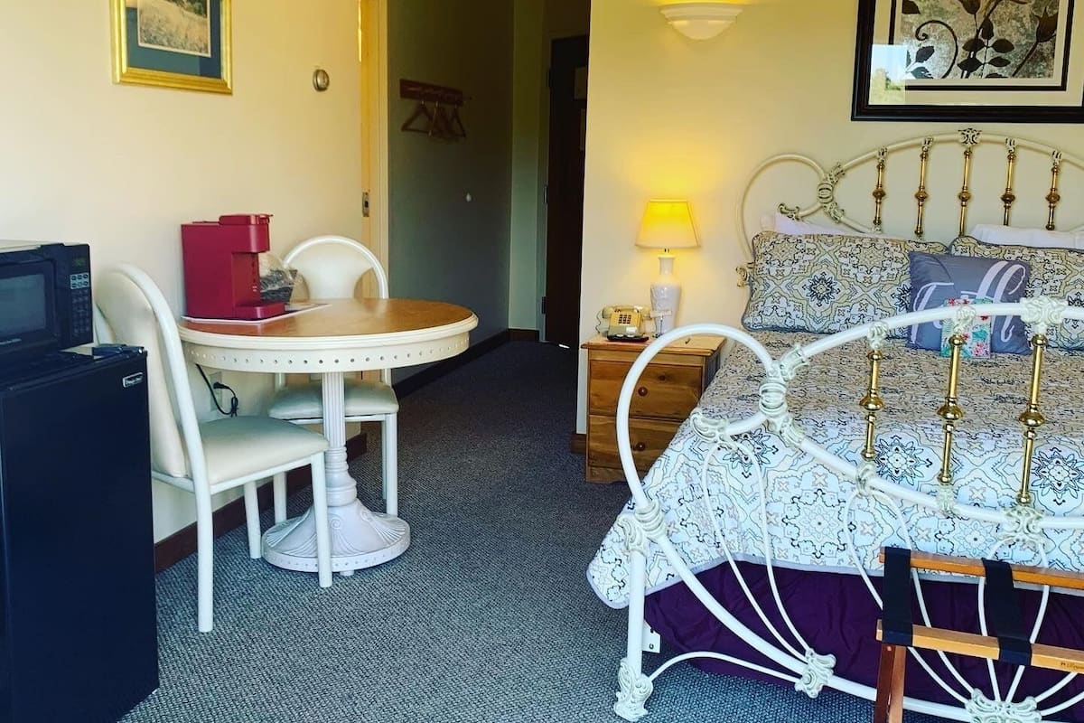 A hotel room with a bed, a desk with a computer, a chair, a small table, and a lamp.