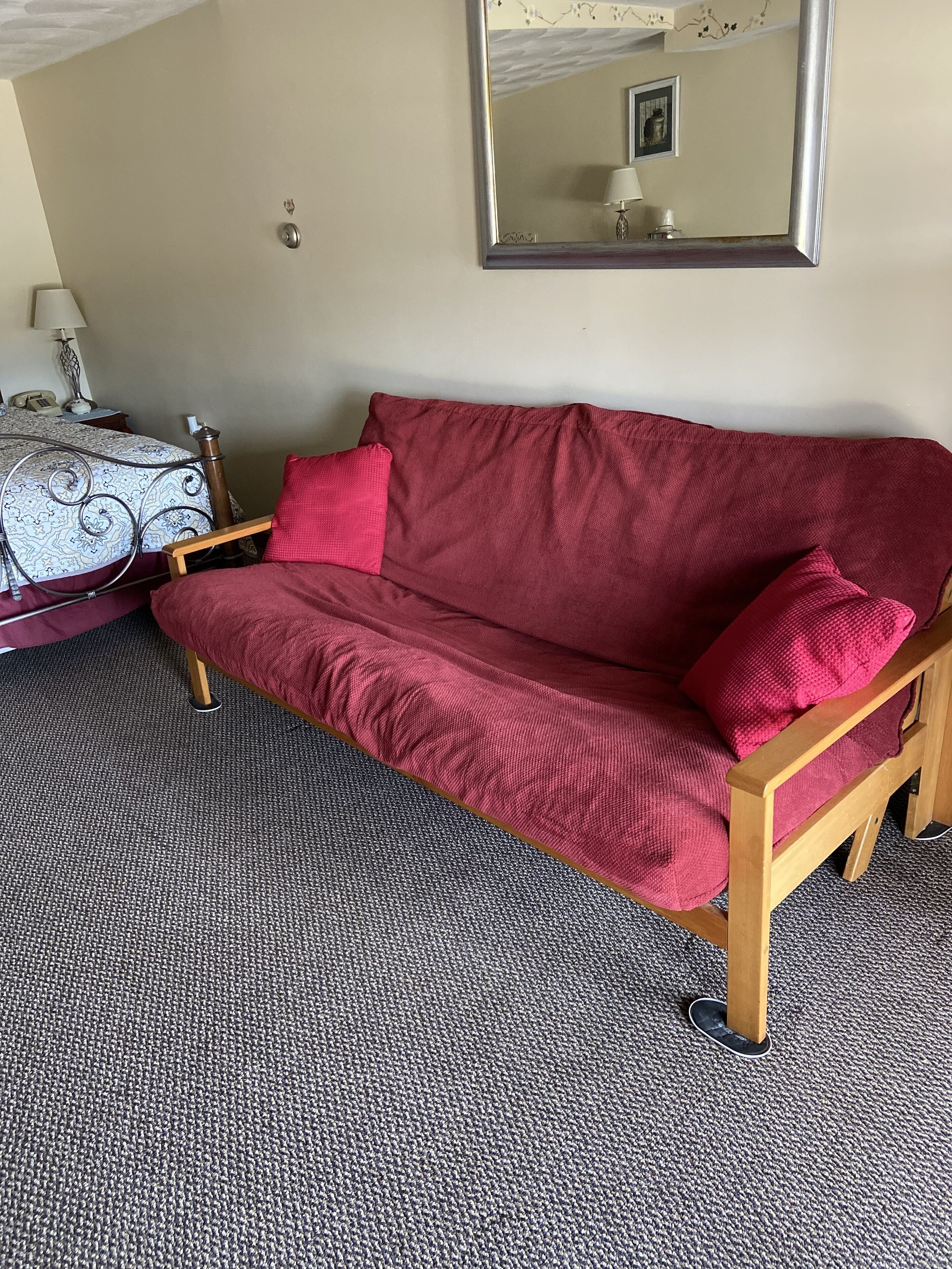 A room with a red sofa, a patterned armchair, a small table with a lamp, and a mirror on the wall.