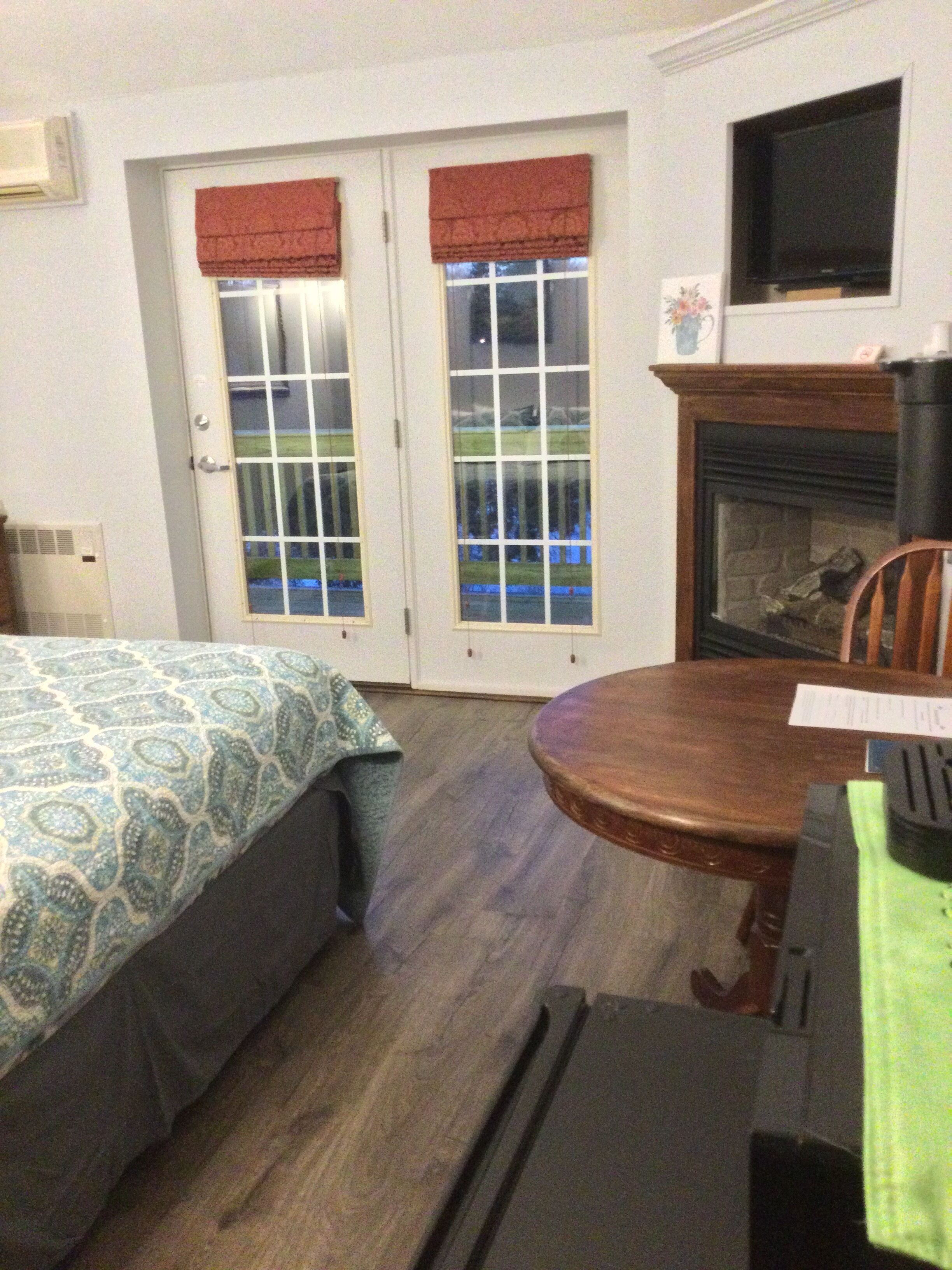 A hotel room with a bed, a dining table, a fireplace, and a view through the windows.
