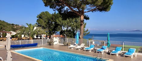 A pool area with lounge chairs and a view of the sea.