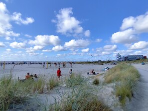 A beach with people, dunes, and a building in the background.
