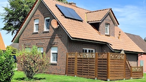 Une maison à deux étages, avec une façade en briques, un toit en pente équipé de panneaux solaires et une clôture en bois.