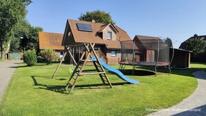Un quartier résidentiel avec une maison, une balançoire, un toboggan et un trampoline.