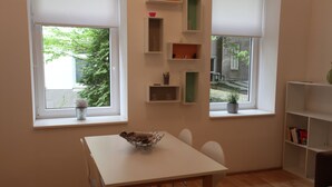 A room with a white table, chairs, a window with a view of greenery, and built-in shelves with various items. - Modern, quiet apartment in an old building (Wien)