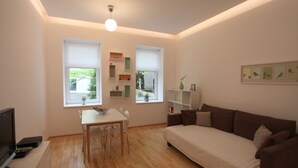 A modern living room with a white sofa, a dining table with chairs, and a TV. - Modern, quiet apartment in an old building (Wien)