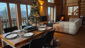 A cozy dining area with a wooden table set for four, a Christmas tree, and a fireplace. - Chalet Asphodel (Haute-Nendaz)